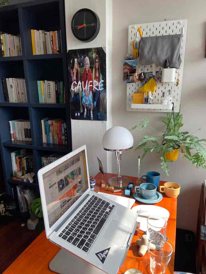 温かみのある木目調のデスクにノートパソコンとヴィンテージの小物が置かれたホームオフィス空間、壁には本棚とペグボードが配置されている