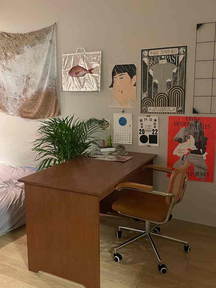 木目調のナチュラルな色合いのホームオフィス、デスクとオフィスチェアが中心で、壁のポスターと植物が配置された温かみのあるインテリア