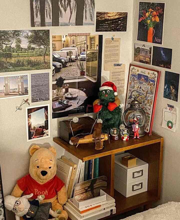 白い壁とブラウンの木製棚がある寝室のコーナー、多彩なクリスマス装飾と壁の写真で飾られた雰囲気のある空間