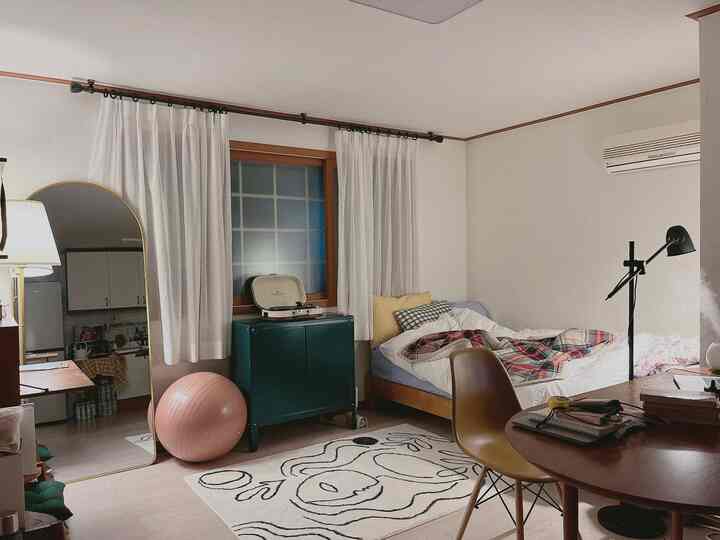 白い壁と木目調の床の寝室、デスク、椅子、ベッド、模様のあるラグが配置された雰囲気のあるインテリア