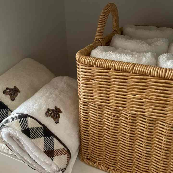 ナチュラルカラーのバスルーム、ラタンバスケットと白いタオルが整頓された印象的な空間