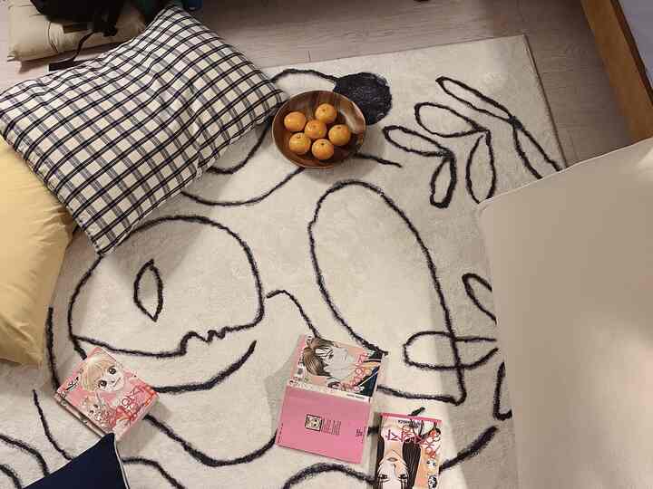 明るいナチュラルトーンの一人暮らし寝室、チェック柄の枕と抽象的なラインのラグ、木製の皿が配置された雰囲気のある空間