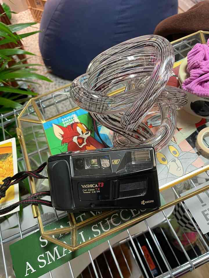 透明なオブジェが置かれたゴールド縁のトレイの上にフィルムカメラがある、ビーズクッションが見える居心地の良いリビングスペース