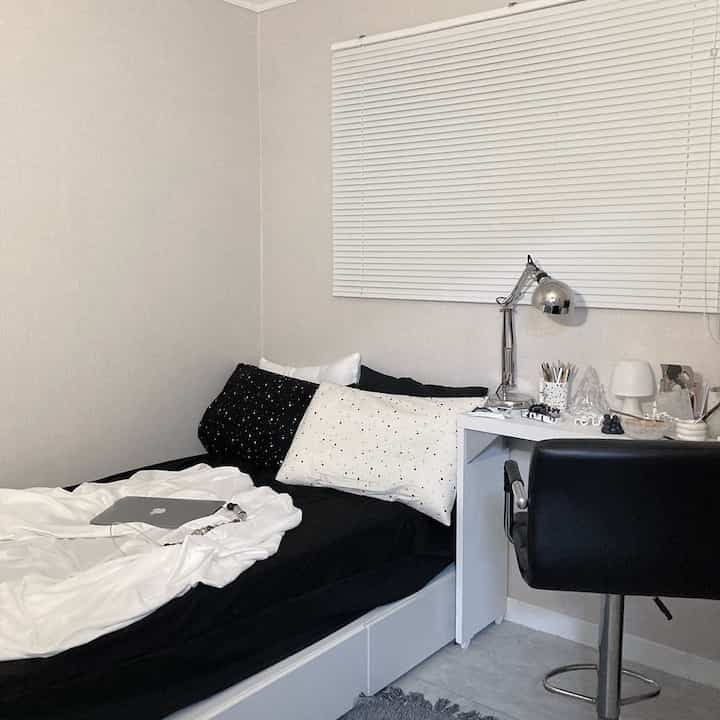 白と黒のトーンの寝室、シングルベッドとデスク、オフィスチェアが配置された落ち着いたコンパクトな空間