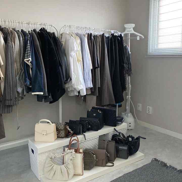 白とグレーの色調のウォークインクローゼット、両側の壁にハンガーラックとバッグ棚が整然と配置された洗練された空間