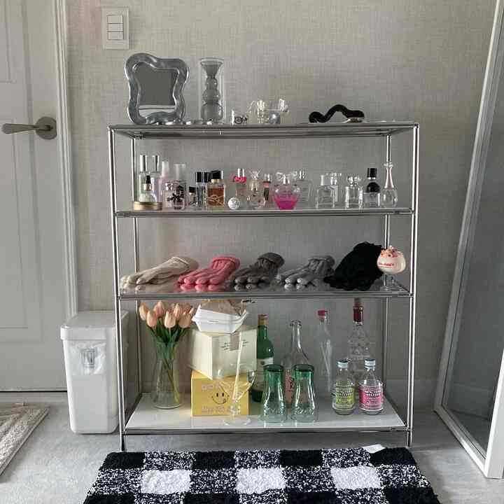 白とグレーの色調のリビングルーム、クローム製の棚に多様な装飾品とピンクのチューリップが配された印象的な空間