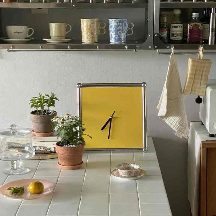 白いタイルのダイニングテーブルがあるキッチン、黄色い時計とマグカップ、植物が配置されたミニマルなインテリア