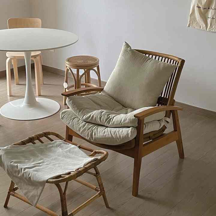 ナチュラルな色調のリビング、木製のアームチェアとスツール、白い円形ダイニングテーブルが配置された雰囲気のあるインテリア