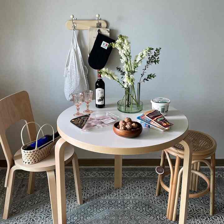 ホワイトとブラウンの色調による円形の部屋、木製のダイニングテーブルとスツール、花の入った花瓶が置かれた自然な雰囲気のインテリア