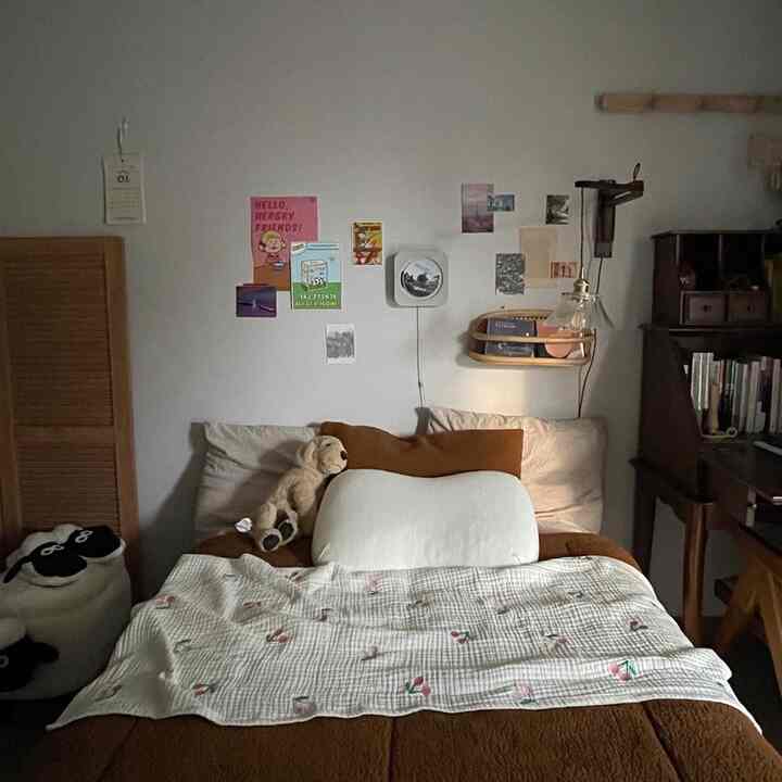 暖かいブラウンと木目調の寝室、中央にベッドと犬のぬいぐるみ、右側に木製デスクが配された落ち着いた空間
