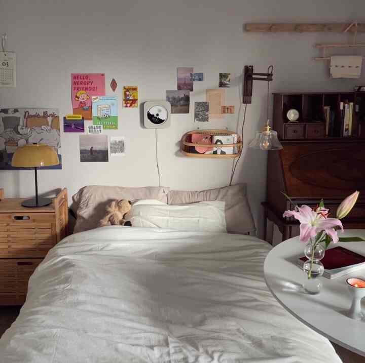 白とナチュラルな色調のコンパクトな寝室、中央にベッドとナイトテーブル、壁にポスターが配置されたシンプルな空間