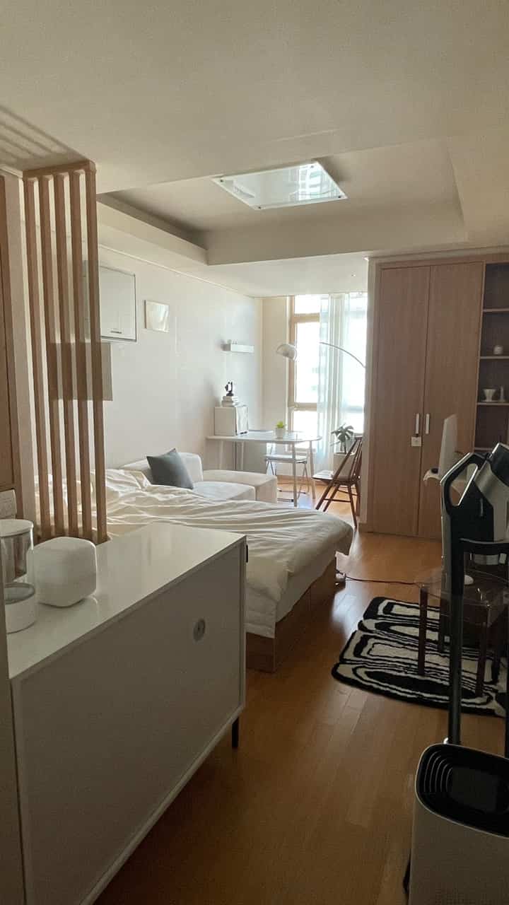 白と木目調が調和した一人暮らしの寝室、ソファと机が配置された落ち着いたコンパクトな空間