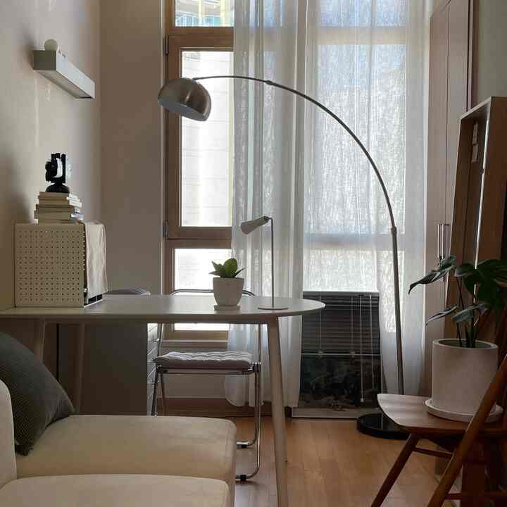 ホワイトとウッドトーンが調和する寝室、窓辺にデスクとフロアランプが配置されたシンプルでナチュラルなインテリア