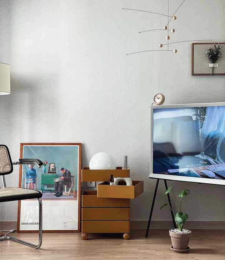 木目調の床とモダンなリビング、マスタード色の収納家具と絵画、テレビ、ダイニングチェアが配されたシンプルなインテリア