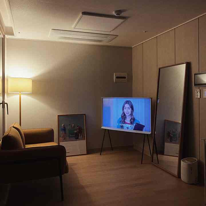 ナチュラルカラーのワンルームリビング、キャメル色の2人掛けファブリックソファ、フロアランプ、テレビスタンド、大きな全身鏡が配置された温かみのある空間