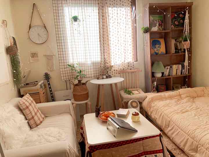 ベージュと木目調が調和する小さなダイニングルーム、ヴィンテージの本棚と柄のカーテン、植物が配置された雰囲気のある空間