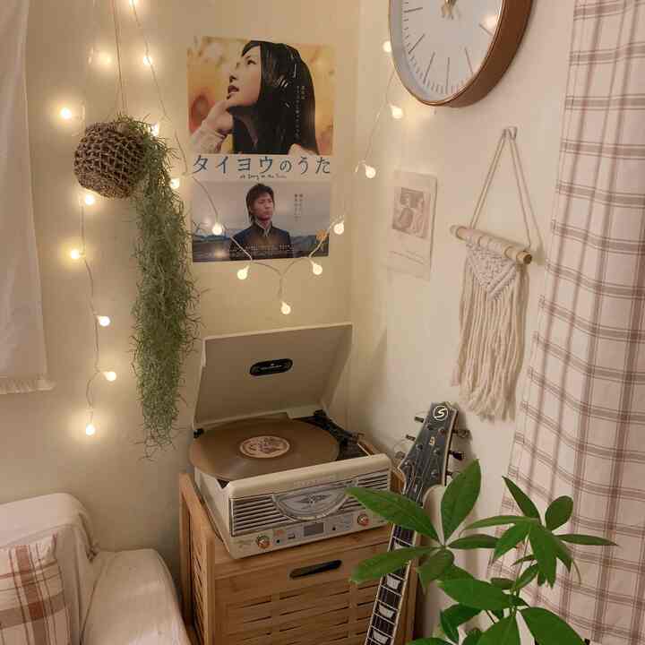 暖かいナチュラルカラーの小さな空間にレトロなLPターンテーブルと植物、マクラメ飾りが配置された居心地の良い音楽鑑賞スペース