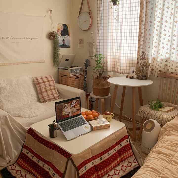 ベージュとホワイトの落ち着いた色調のリビング、こたつテーブルやソファ、植物、カーテンが配置された雰囲気のある空間