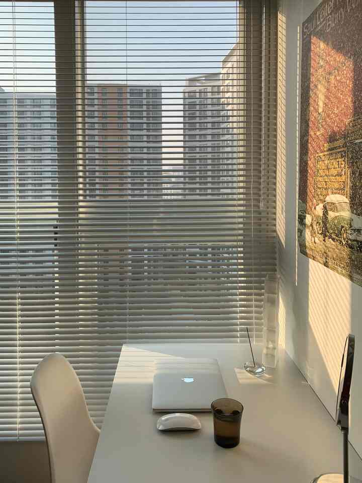 白を基調としたホームオフィス、すっきりとしたデスクと椅子、ブラインドで覆われた窓から温かい日差しが差し込む雰囲気のあるインテリア