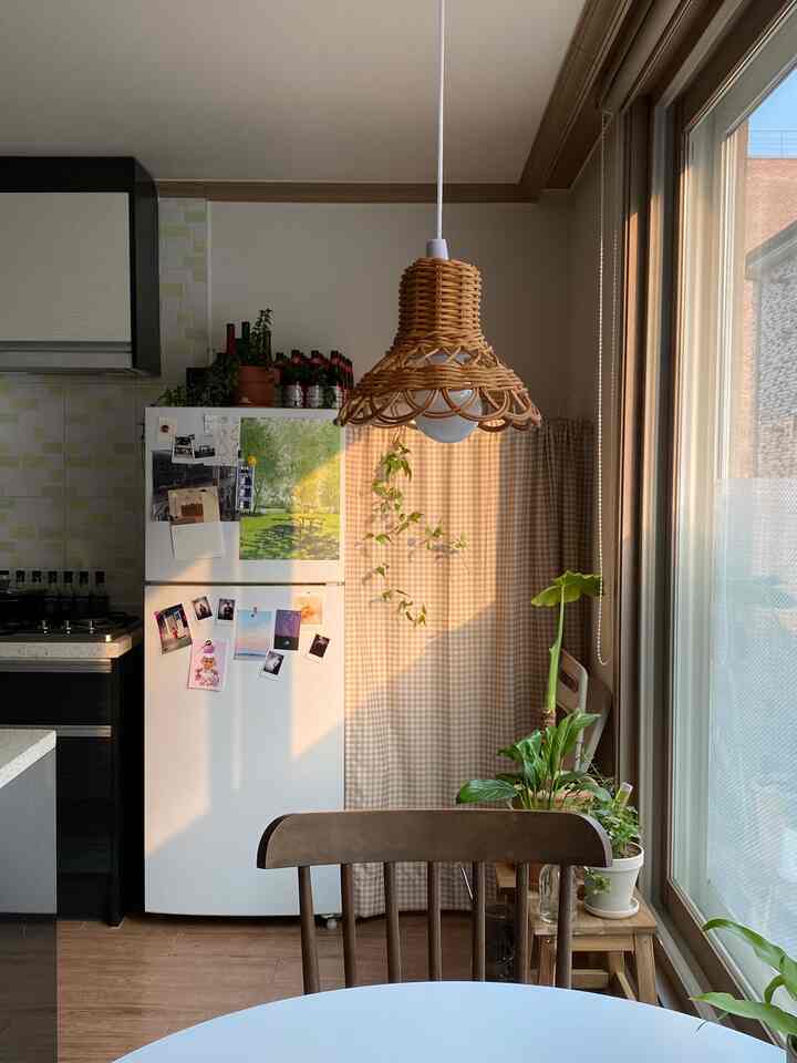 暖かいウッドトーンとベージュのチェックカーテンが配された、心地よいキッチン空間。ダイニングチェアや複数の植物が配置されている雰囲気のあるインテリア