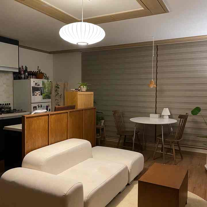 暖かいウッドトーンと電球色の照明が調和したリビングとキッチン、白いソファと丸いダイニングテーブルが配置されたアットホームな空間