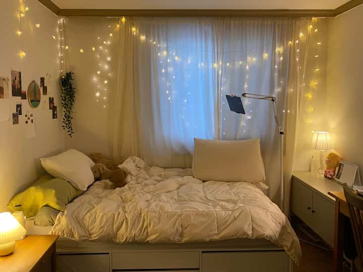 暖かいイエローライトとホワイトカーテンがあるナチュラルな色調の寝室、居心地よく照明が際立つ空間