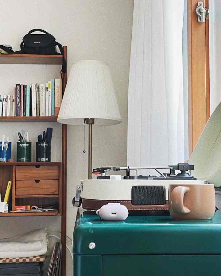 ナチュラルな色調のリビングコーナー、レトロなLPプレーヤーと木製の棚、フロアランプが配置された雰囲気のある空間