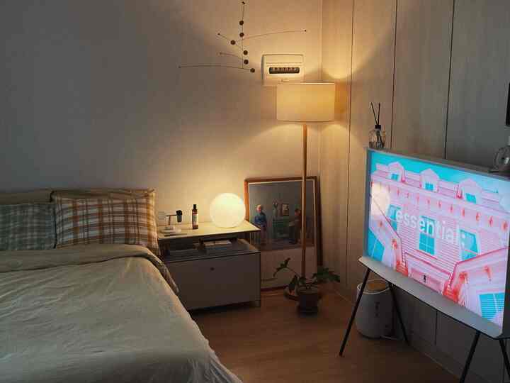 暖かいナチュラルトーンの寝室、ベッドとフロアランプ、テレビ台が配置された雰囲気のあるインテリア