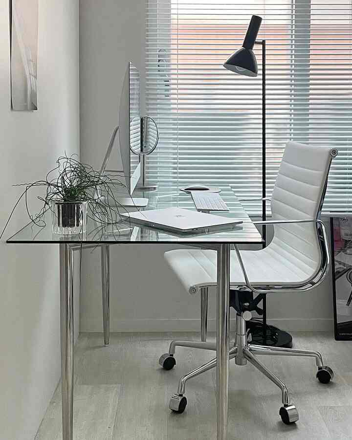 ホワイトとグレーのトーンのホームオフィス、ガラスのデスクとオフィスチェアが配置された清潔感のある作業空間