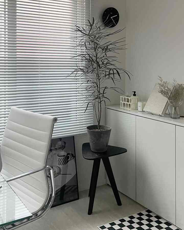 白とダークグレーの色調のホームオフィス空間、オフィスチェアとスツールの上の植物が配置されたシンプルなインテリア