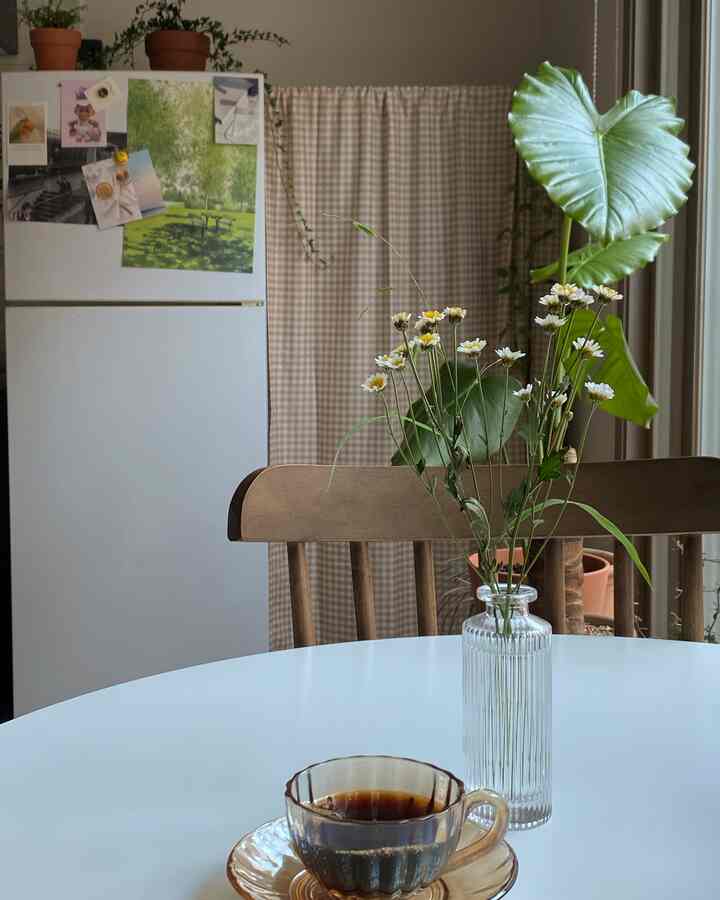 柔らかなホワイトとブラウンのトーンが特徴のキッチン・ダイニングスペース、丸いテーブルにガラスの花瓶とコーヒーカップが並ぶ雰囲気のあるカフェ風インテリア