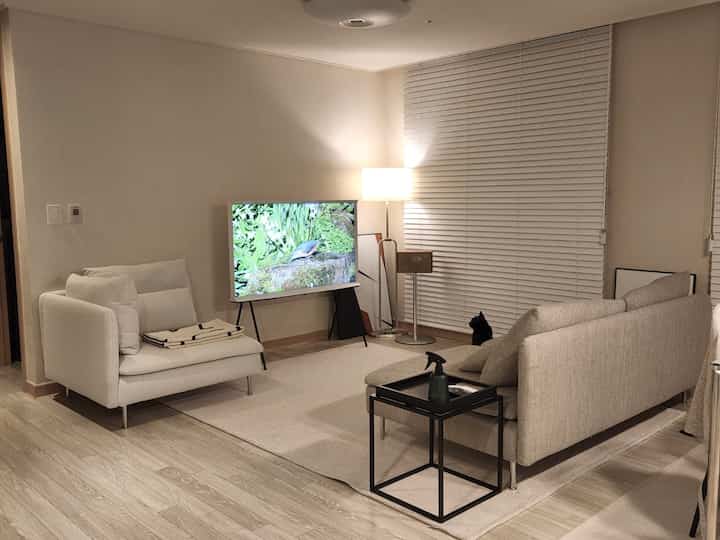 アイボリーとベージュのトーンのリビング、アームチェアとベージュのソファ、白いブラインドが配置された雰囲気のあるモダンな空間