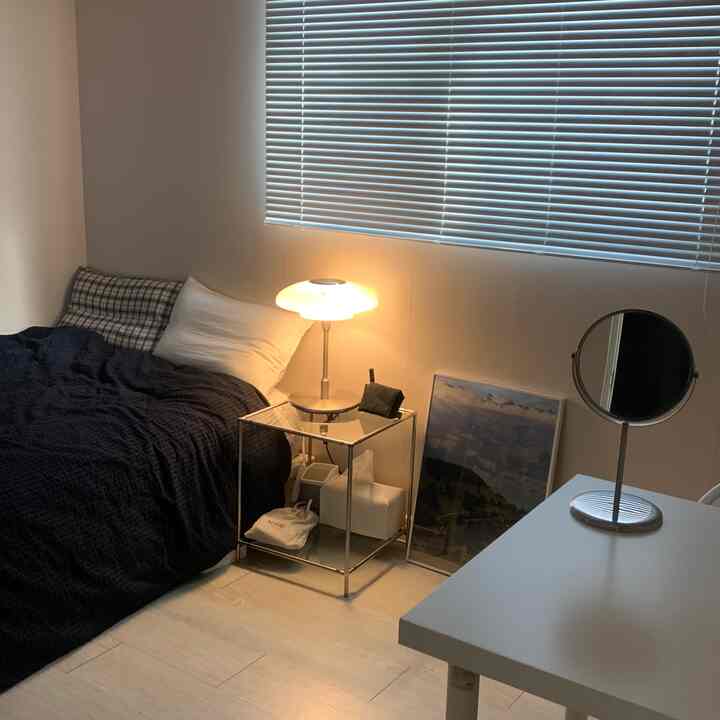 白い壁とブラインドのある寝室、ネイビーベッドリネンとミッドセンチュリーモダンのナイトテーブルと照明が配置された落ち着いた空間