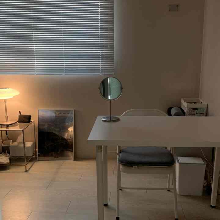 白とベージュのトーンのホームオフィス、机と椅子、サイドテーブルと照明が落ち着いた雰囲気を演出する空間