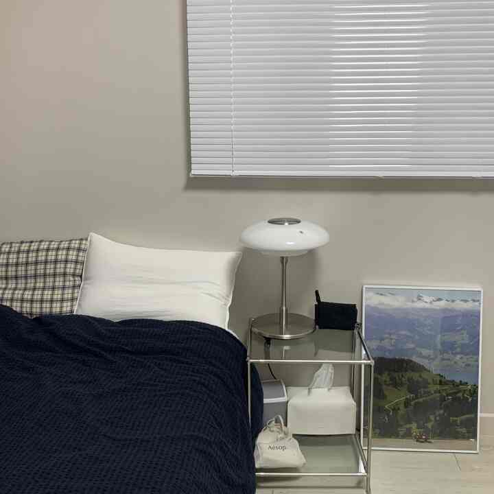 白とネイビーの色調の寝室、ナイトテーブルとテーブルランプ、ブラインドが配置された雰囲気のあるインテリア