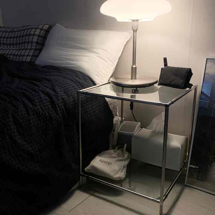 ホワイトの壁とネイビーブルーの寝具があるシンプルな寝室、メタルフレームのナイトテーブルとテーブルランプが配置された落ち着いたインテリア