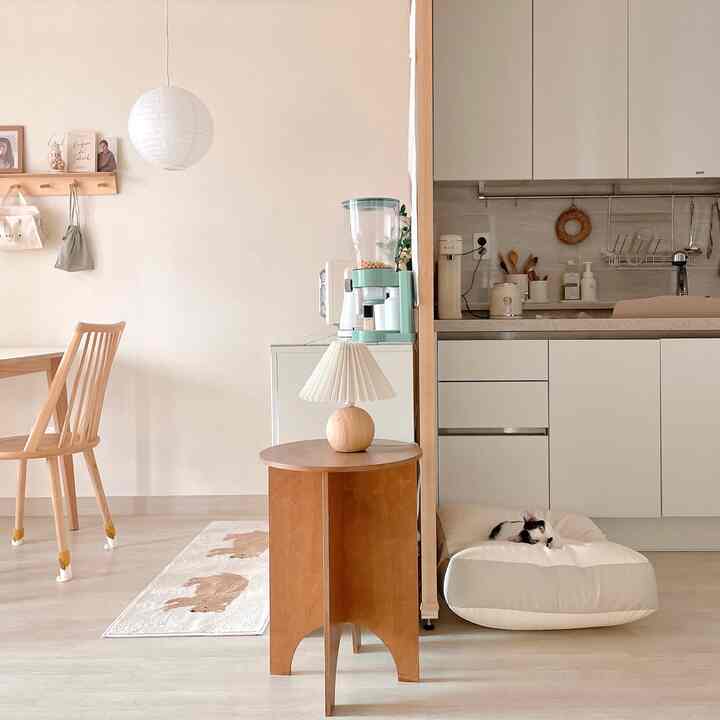 白とベージュのトーンのキッチンとリビングスペース、自然な木材家具と猫用ペットベッドが配置されたシンプルな雰囲気のインテリア
