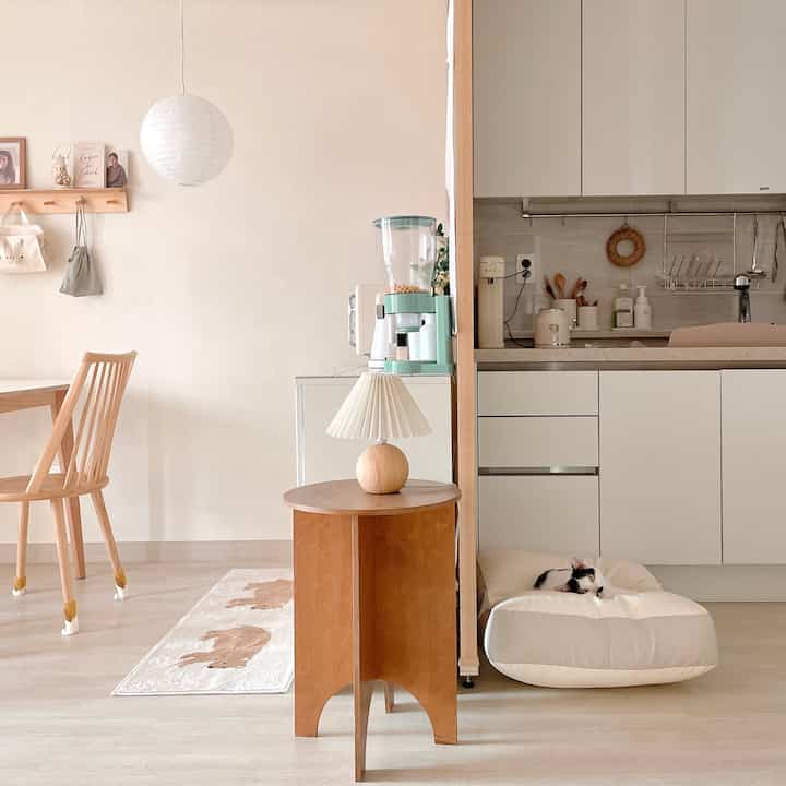 ナチュラルな色調のリビングとキッチン、木製家具と間仕切り、猫用クッションが置かれた温かみのあるインテリア