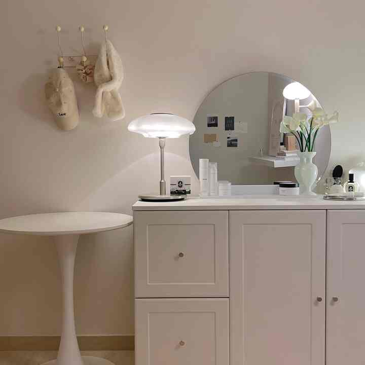 白とベージュのトーンの化粧台空間、丸い鏡とテーブルランプが温かい雰囲気を演出するすっきりとしたインテリア