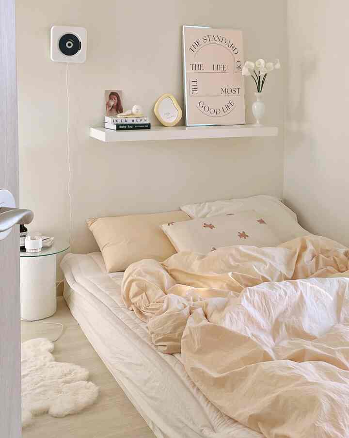 温かみのあるベージュ調の寝室、低いベッドと白い浮遊棚が配置された雰囲気あるインテリア