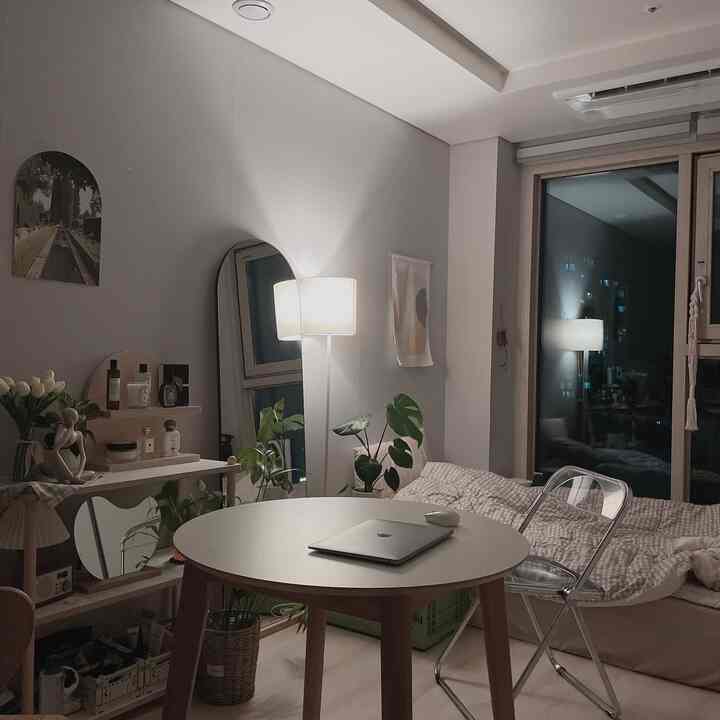 白と木目調が調和したワンルーム寝室、丸いダイニングテーブルと透明な椅子、フロアランプが印象的な空間を作り出す