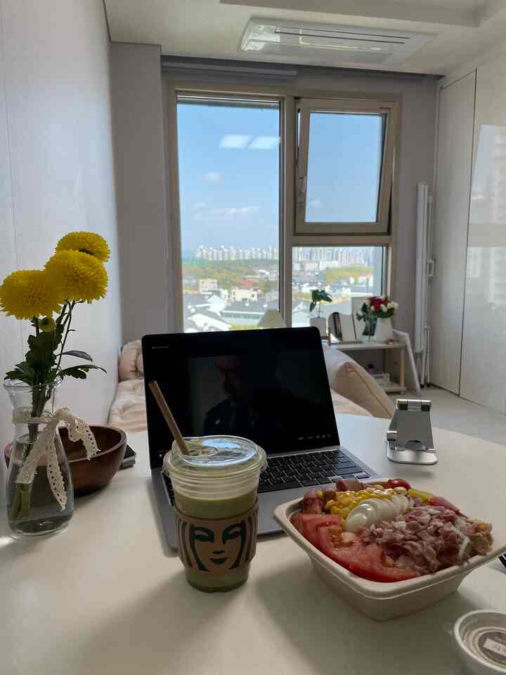 明るい白を基調とした7坪の小さなダイニングルーム、中央にテーブルとノートパソコン、飲み物が置かれ、大きな窓から街の景色が見える印象的な空間