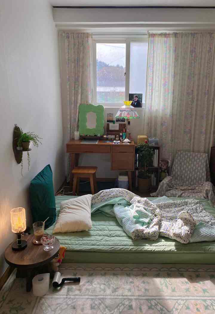 アイボリーの壁のある小さな寝室、グリーンの寝具とヴィンテージ家具が配置された雰囲気のある空間