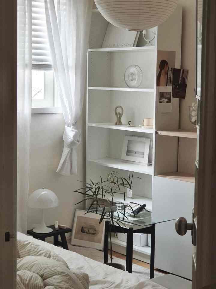 白とベージュの色調の寝室、中央に本棚が配置され、シンプルなインテリアが印象的な空間