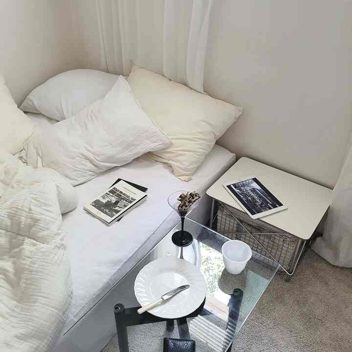 白とナチュラルな色調の寝室、ベッドとナイトテーブルが配置された印象的な開放感あるインテリア