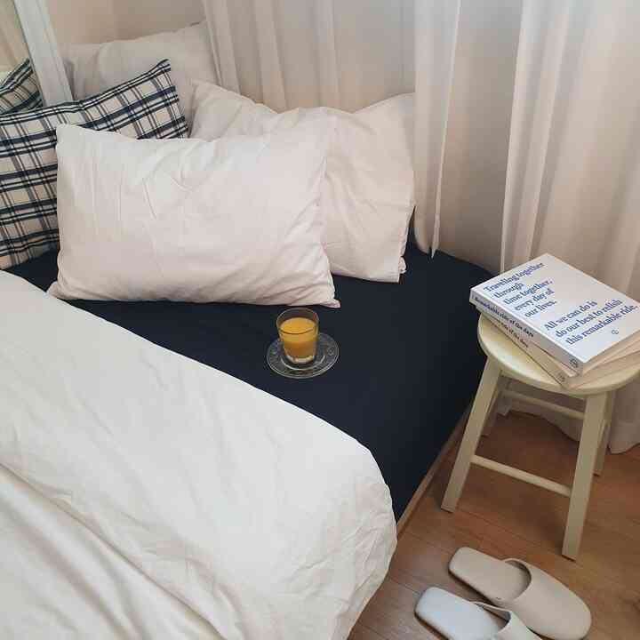 白とネイビーのトーンが特徴の寝室、マットレスとクッション、小さなサイドテーブルとカーテンが配置された印象的な空間