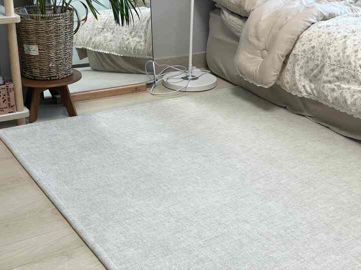 明るいベージュ調の寝室空間、大きなカーペットと木製スツールが配置された自然で温かみのあるインテリア