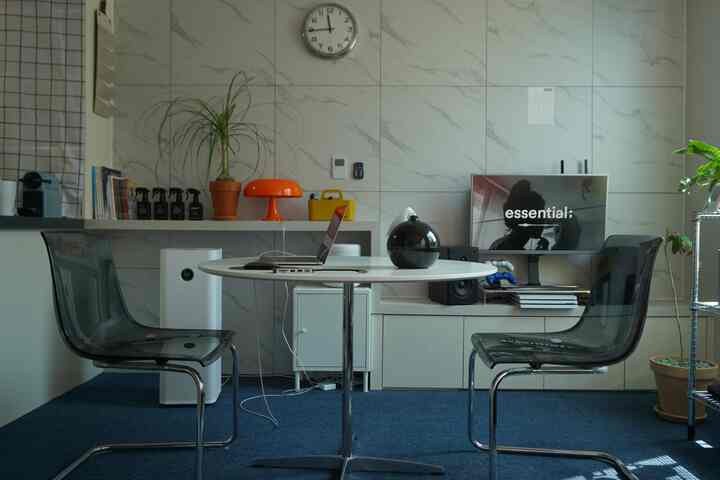 モダンでコンパクトな一人暮らしリビング、透明な椅子と丸いテーブル、植物とオレンジ色のテーブルランプが配置された実用的な空間