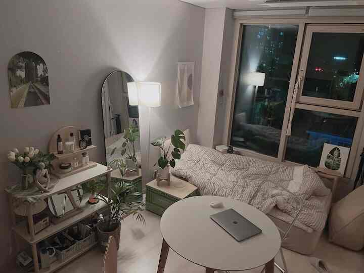 白とベージュの色調が特徴の一人暮らし用の小さな部屋、ベッドと丸いダイニングテーブルが配置された雰囲気のあるナチュラルモダンなインテリア