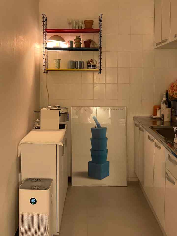 白を基調とし、多彩な色の棚とポスターが配置されたコンパクトなキッチンの雰囲気のあるインテリア